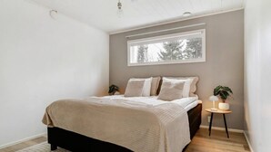 Et soveværelse med seng, et vindue, et natbord med lampe og en lille plante.