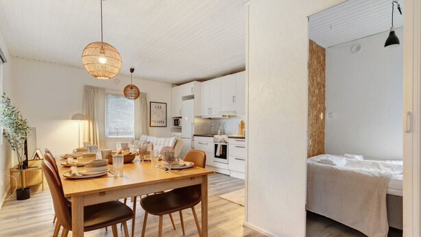 Et moderne køkken med hvide skabe, et træspisebord og en hængende lampe.