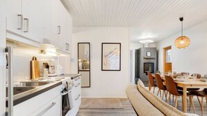 Et moderne køkken med hvide skabe, indbygget ovn og spiseplads med bænk og stole.