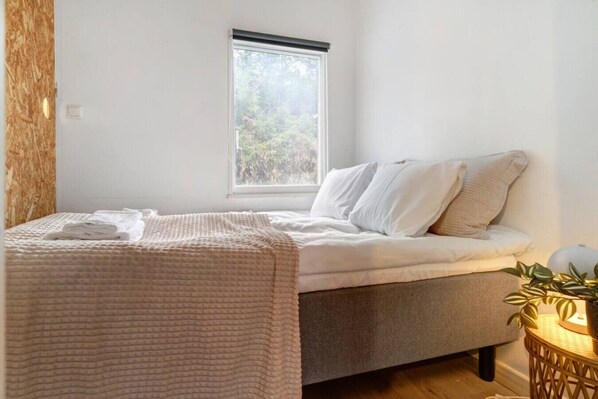 A bedroom with a bed, a window, and a bedside plant.