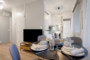 Un espace repas moderne avec une table ronde pour quatre personnes, un téléviseur et une cuisine en arrière-plan.