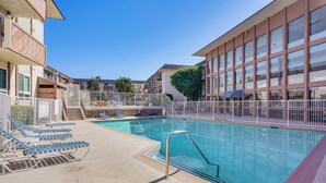 A swimming pool with lounge chairs and a covered seating area, surrounded by buildings with balconies and windows. - Steps to CSULB: Cozy Condo w/ Pool Access! (Long Beach)