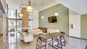 A spacious, well-lit interior with a high ceiling, a stone accent wall, a large dining table, and modern furnishings. - Steps to CSULB: Cozy Condo w/ Pool Access! (Long Beach)