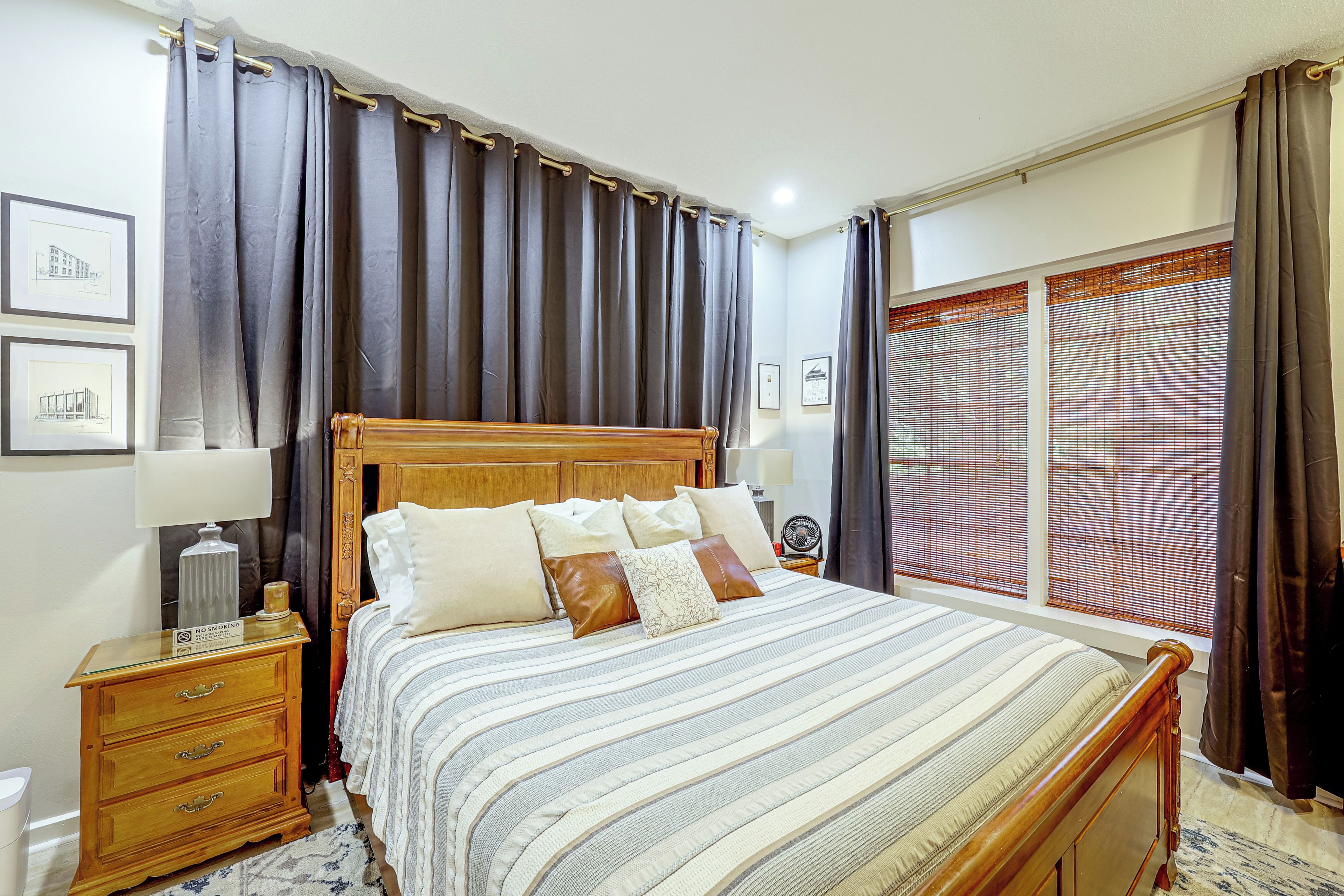 A bedroom with a wooden bed, a nightstand, a lamp, a bedside table with a candle, and a window with blinds.