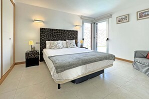 Quarto com cama grande, cabeceira com padrão circular, duas luminárias de cabeceira e vista para o exterior por uma porta de correr de vidro.