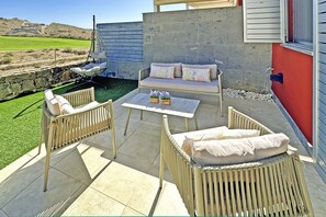 An outdoor patio with wicker furniture, a cushioned sofa, and a hanging chair. - Salobre Vista Golf 24 (Maspalomas)