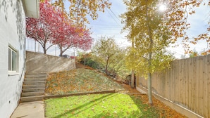 Un jardin à l’arrière d’une maison, avec une pelouse verdoyante, une clôture en bois et un escalier menant à un bâtiment blanc.