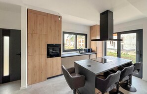 Une cuisine moderne avec des meubles en bois, un four encastré, une grande fenêtre et un îlot central doté de tabourets de bar.