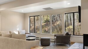 A modern living room with a large window, a sofa, a chair, and a small table. - Fallridge Condo - Close to Bus & Nordic Center (Vail)