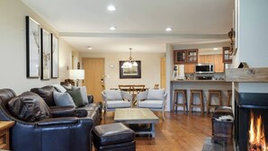 A living room with a fireplace, a dining area, and a kitchen with wooden cabinets. - Fallridge Condo - Close to Bus & Nordic Center (Vail)