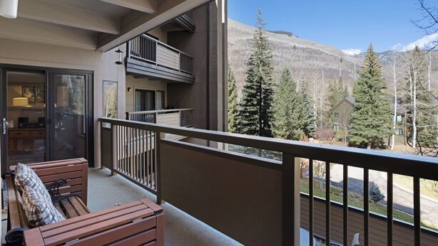A balcony with a view of a mountainous landscape, a wooden bench, and a glass door leading to an interior space. - Fallridge Condo - Close to Bus & Nordic Center (Vail)