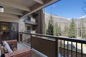 Ein Balkon mit Blick auf eine Berglandschaft, eine hölzerne Bank und eine Glastür zu einem Innenraum.