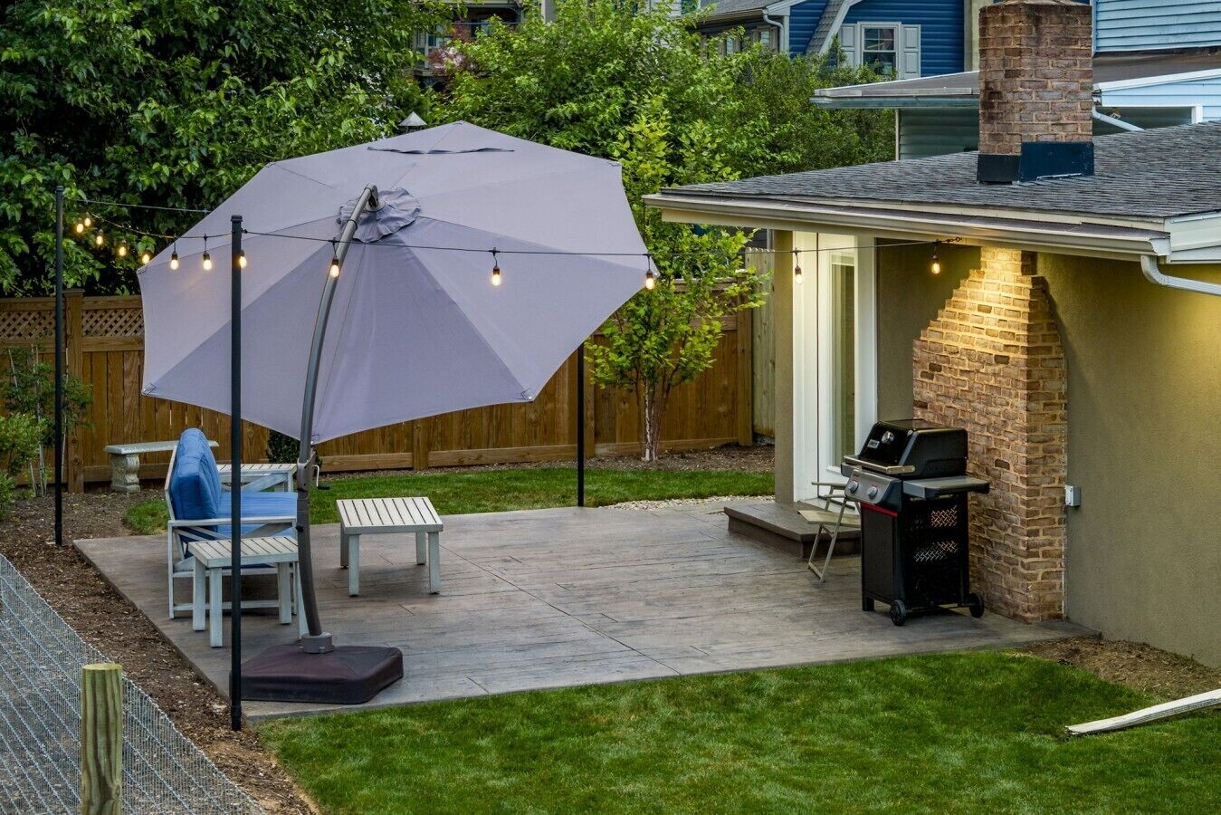 An outdoor patio with a grill, a table, chairs, and a large umbrella.
