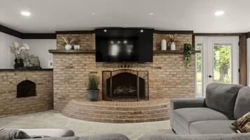 A living room with a stone fireplace, a flat-screen TV mounted above it, and a grey sofa.