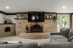 Ein Wohnzimmer mit Kamin aus Stein, einem darüber montierten Flachbildfernseher und einem grauen Sofa.