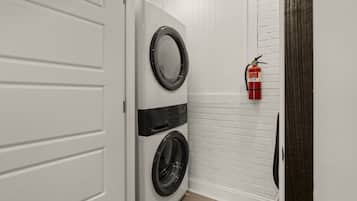 A laundry room with two stacked front-loading washers and a fire extinguisher mounted on the wall.