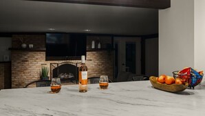 A marble table with glasses and a bottle, a bowl of fruit, and a brick fireplace in the background. - Farm Views | 10min to Sight & Sound (Ronks)