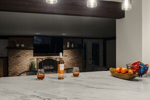 A marble table with glasses and a bottle, a bowl of fruit, and a brick fireplace in the background. - Farm Views | 10min to Sight & Sound (Ronks)