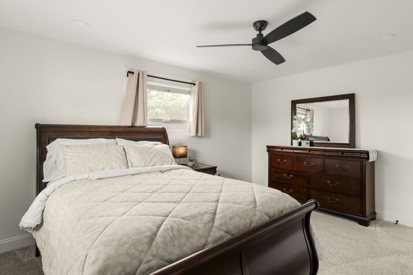 A bedroom with a bed, a dresser, a ceiling fan, and a window with curtains.