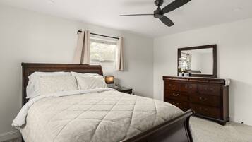 A bedroom with a bed, a dresser, a ceiling fan, and a window with curtains.