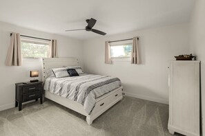 Ein Schlafzimmer mit Bett, Nachttisch, Lampe, Deckenventilator, Fenstern und einem Kleiderschrank.