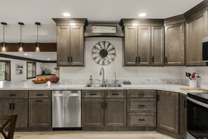 A kitchen with dark wood cabinets, a stainless steel dishwasher, a large wall clock, and pendant lighting. - Farm Views | 10min to Sight & Sound (Ronks)