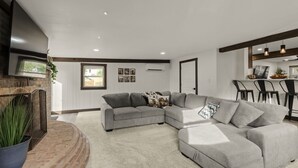 A modern living room with a sectional sofa, a fireplace, and a dining area with bar stools. - Farm Views | 10min to Sight & Sound (Ronks)