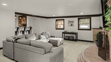 A living room with a grey sectional sofa, a small table, and a TV mounted on the wall.