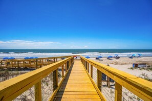 A wooden boardwalk leading to a beach with umbrellas and beach chairs.