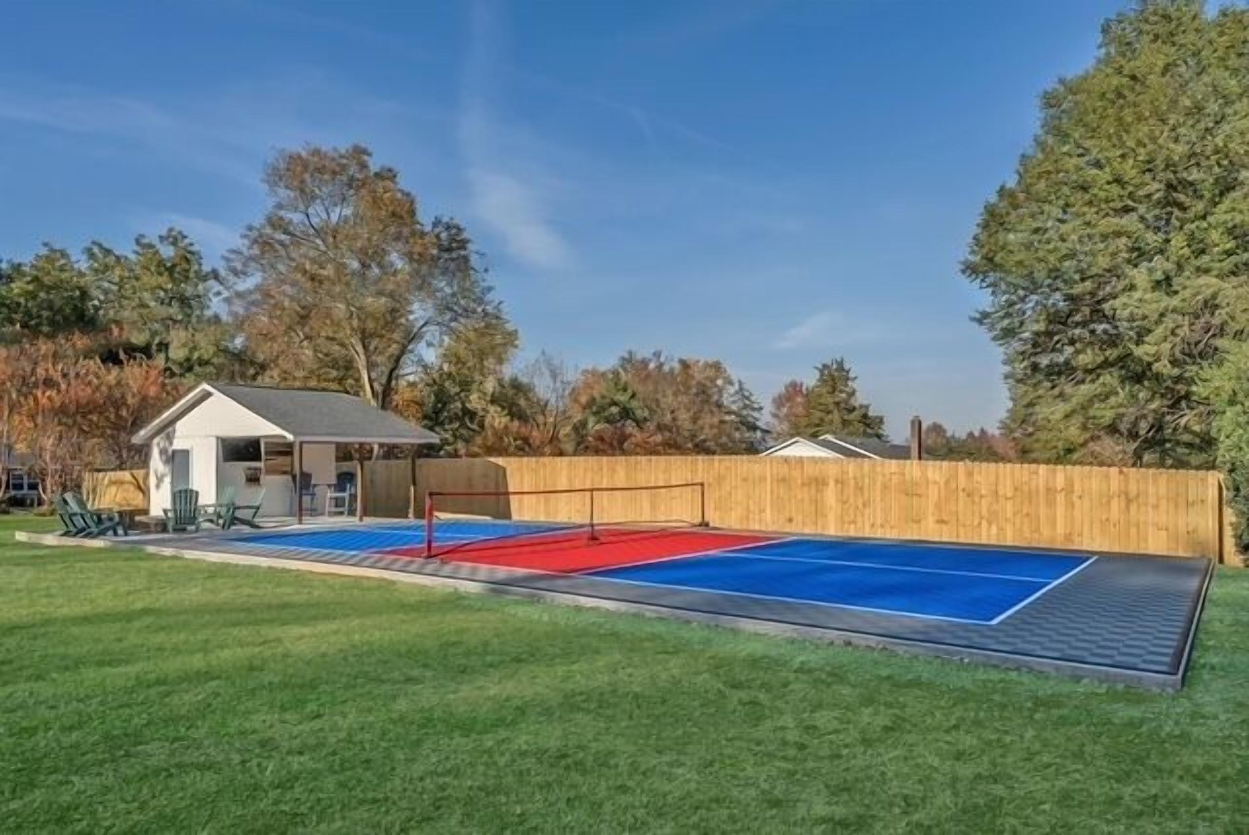 A backyard with a tennis court, a small shed, and a wooden fence.