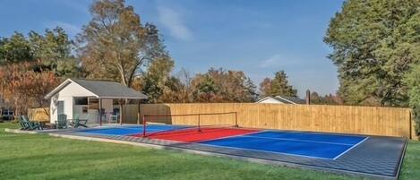 A backyard with a tennis court, a small shed, and a wooden fence.