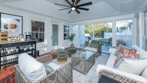 A sunlit room with wicker furniture, a ceiling fan, and a coffee station.