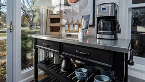 A kitchen counter with a coffee maker, a coffee pot, and a coffee grinder. There are also bottles of coffee and a bag of coffee beans.