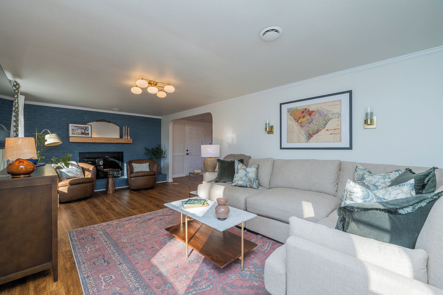 A living room with a sofa, coffee table, and a rug. There is a fireplace, a map on the wall, and a lamp.