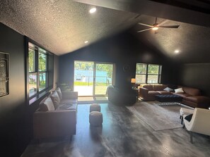 A spacious living room with a high ceiling, large windows, and a view of the outdoors.