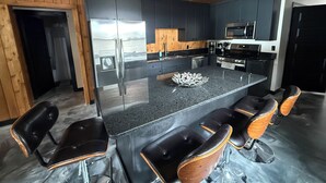 Una cocina moderna con una isla central, asientos tipo barra y electrodomésticos integrados.