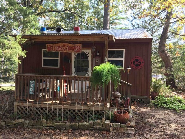 A rustic cabin with a porch, a welcome sign, and a small garden area.