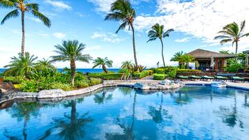 A resort pool with palm trees, a lounge area, and a view of the ocean.