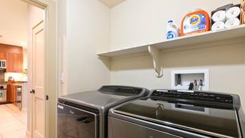 A laundry room with a Whirlpool washer and dryer, a shelf with Tide detergent, and a microwave in the adjacent kitchen.