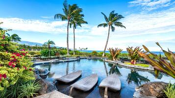 A pool with lounge chairs, palm trees, and a view of the ocean.