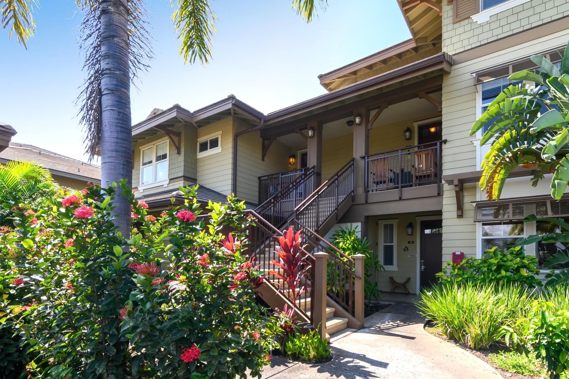 A multi-story residential building with a covered porch, a staircase, and a well-maintained garden with various plants and flowers.