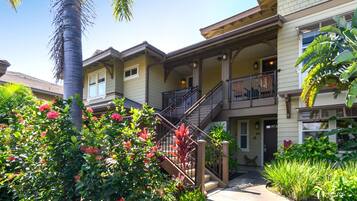 A multi-story residential building with a covered porch, a staircase, and a well-maintained garden with various plants and flowers.