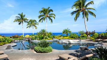 A resort pool area with palm trees, lounge chairs, and a view of the ocean.