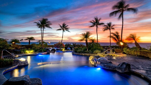 Un espace piscine agrémenté de palmiers et offrant une vue sur le coucher de soleil.