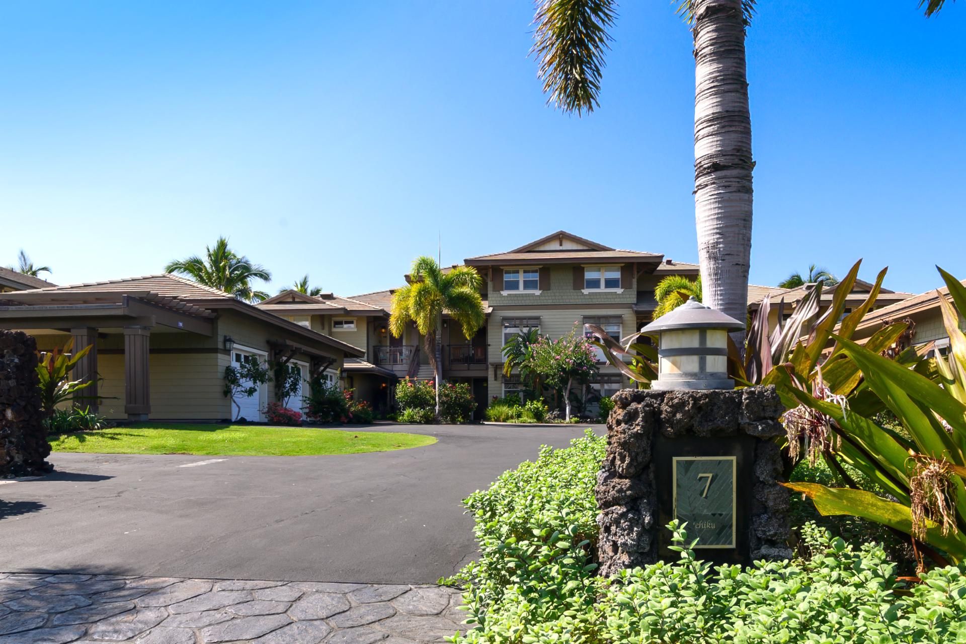 A residential area with a two-story house, a stone pillar with a number plaque, and a well-maintained lawn.