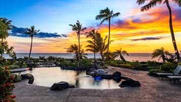A resort with a swimming pool, lounge chairs, and palm trees.