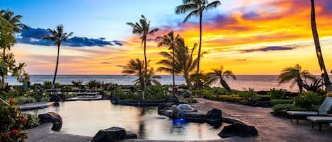 A resort with a swimming pool, lounge chairs, and palm trees.