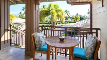 A covered outdoor seating area with a round table and two chairs, a railing, and a view of palm trees and buildings.
