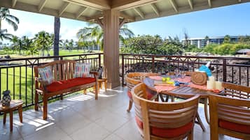 Un espace extérieur abrité, doté d’un banc en bois, d’une table à manger avec des chaises, et offrant une vue sur un terrain de golf et des bâtiments en arrière-plan.