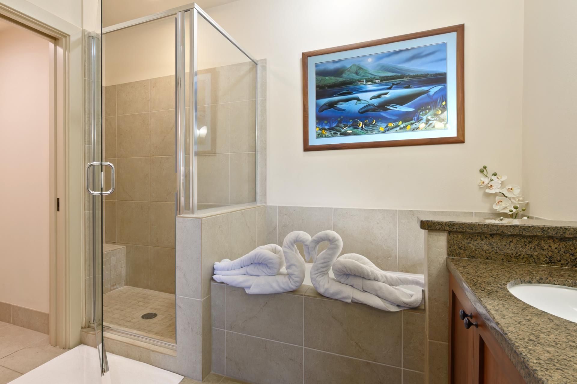 A bathroom with a glass shower enclosure, a framed picture on the wall, and towels on a shelf.